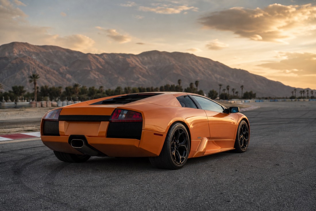 An orange supercar parked on a desert racetrack at golden hour